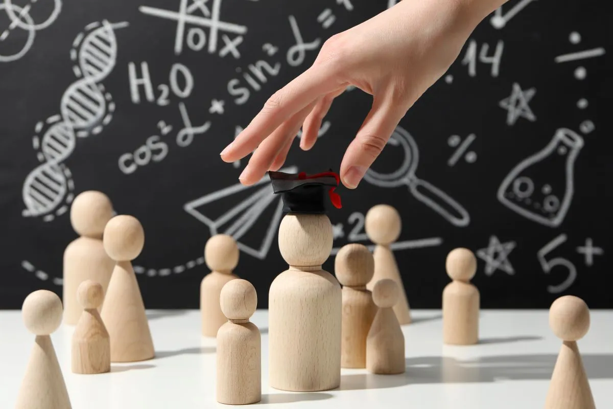 wooden figurines depicting supply teachers and being picked by a hand in front of a chalkboard